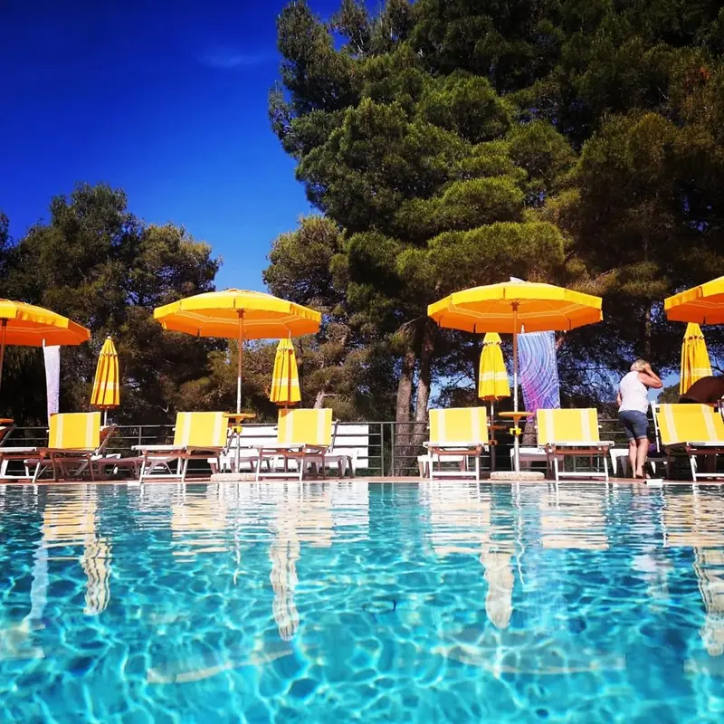 Transats et parasols oranges bordent une piscine bleu clair sous un ciel azur.