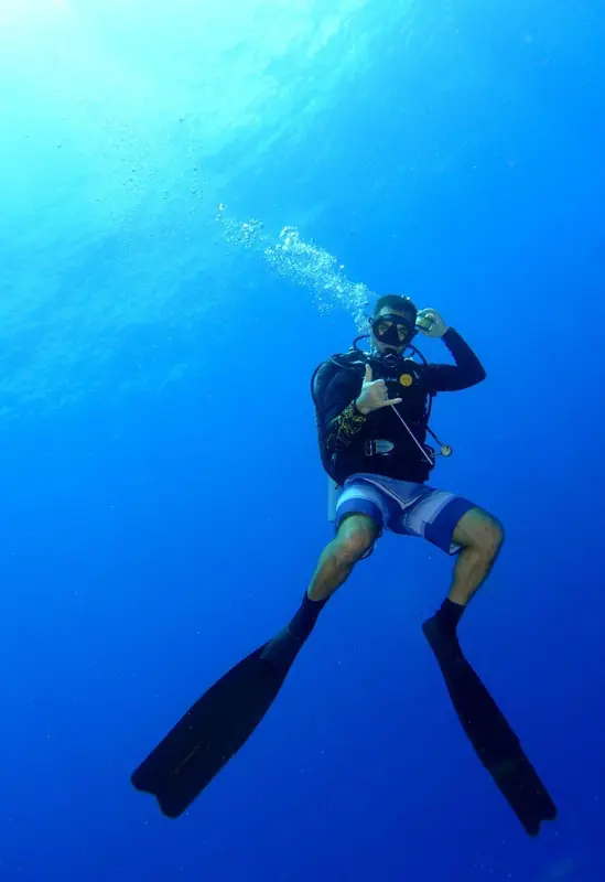 Un plongeur en scaphandre évolue dans une eau turquoise.