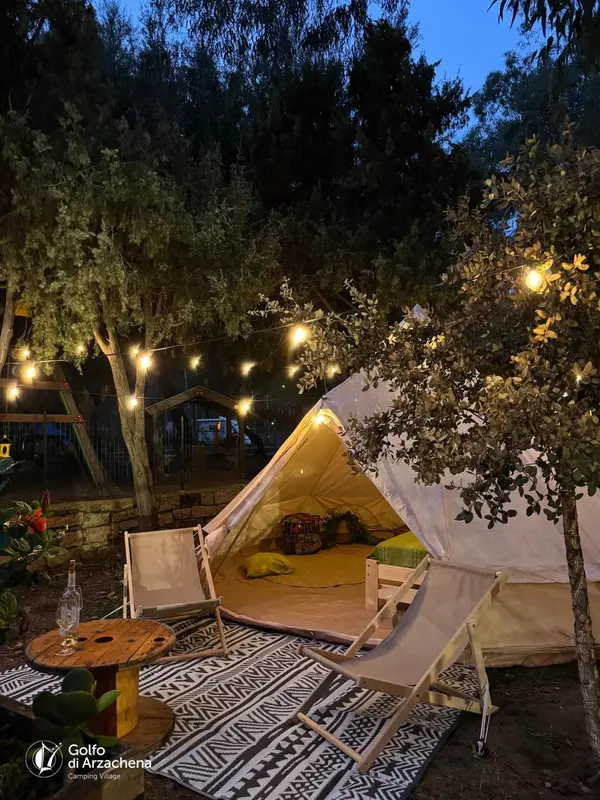 Tente de camping éclairée par des guirlandes lumineuses sous des arbres.