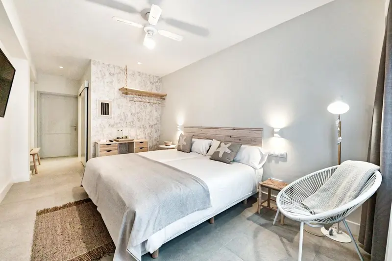 Une chambre lumineuse avec un grand lit et un fauteuil en osier.
