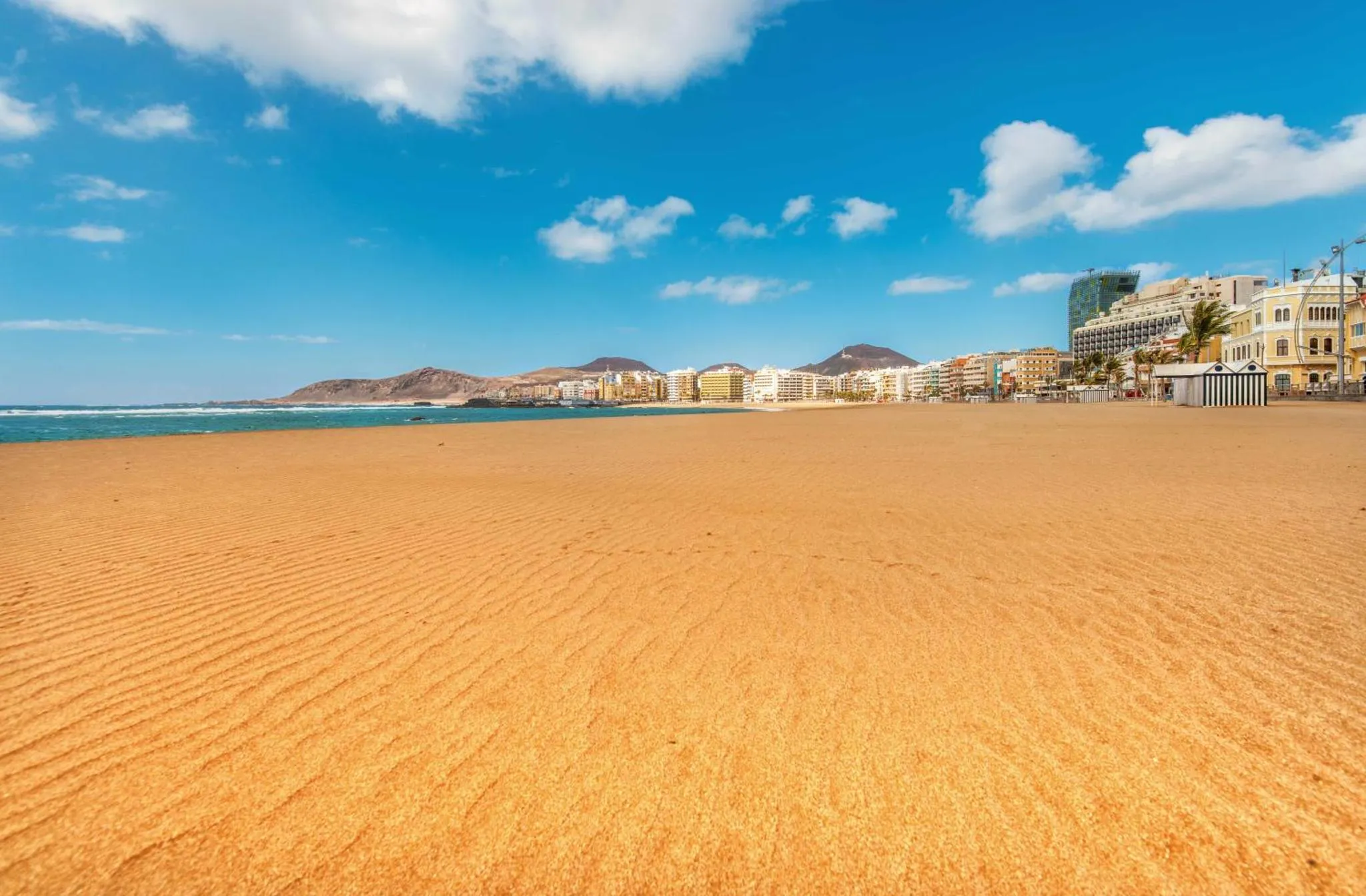 Vaste plage de sable fin bordée par une mer bleue et une ville côtière.