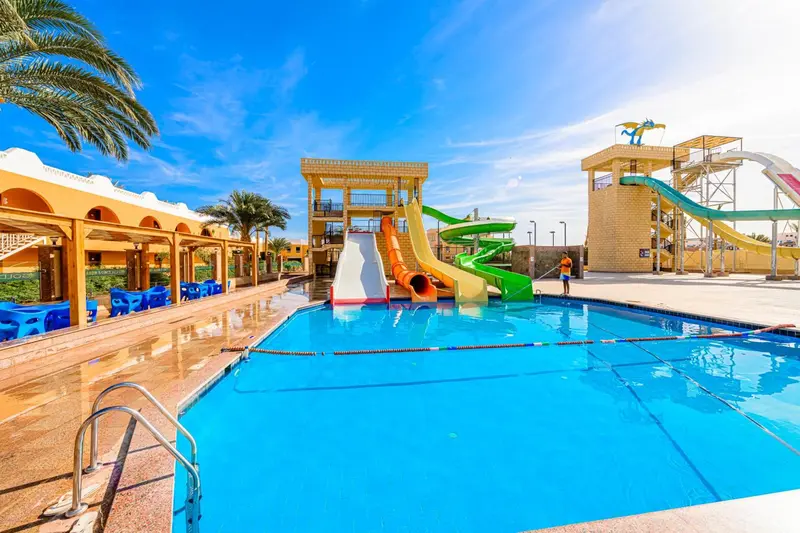 Une piscine turquoise avec toboggans colorés et palmiers en arrière-plan.