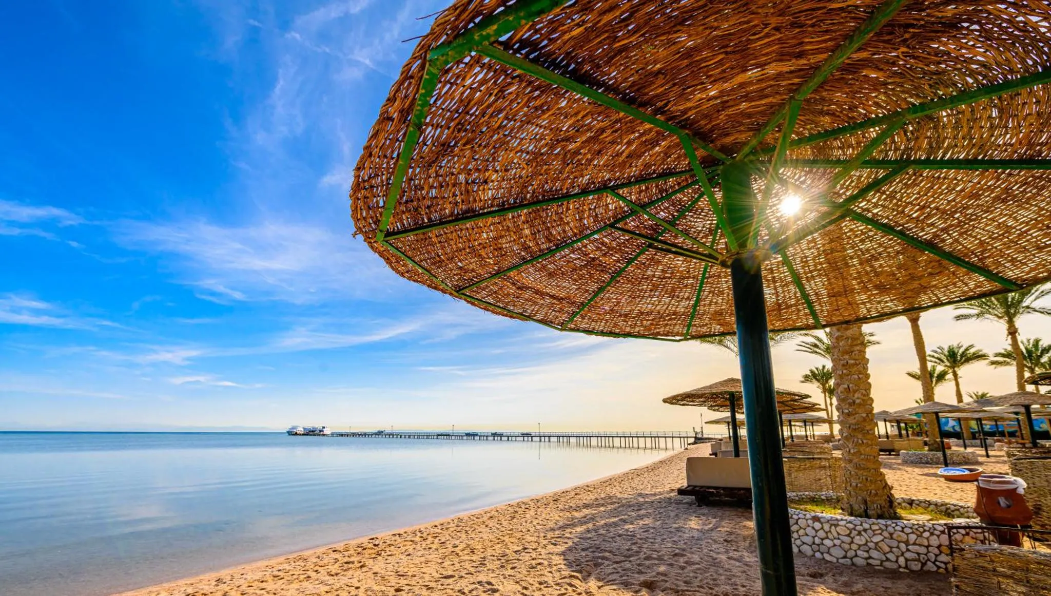 Parasols en chaume sur une plage de sable fin avec vue sur la mer.