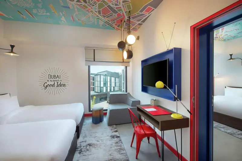 Chambre lumineuse avec deux lits et un espace bureau.