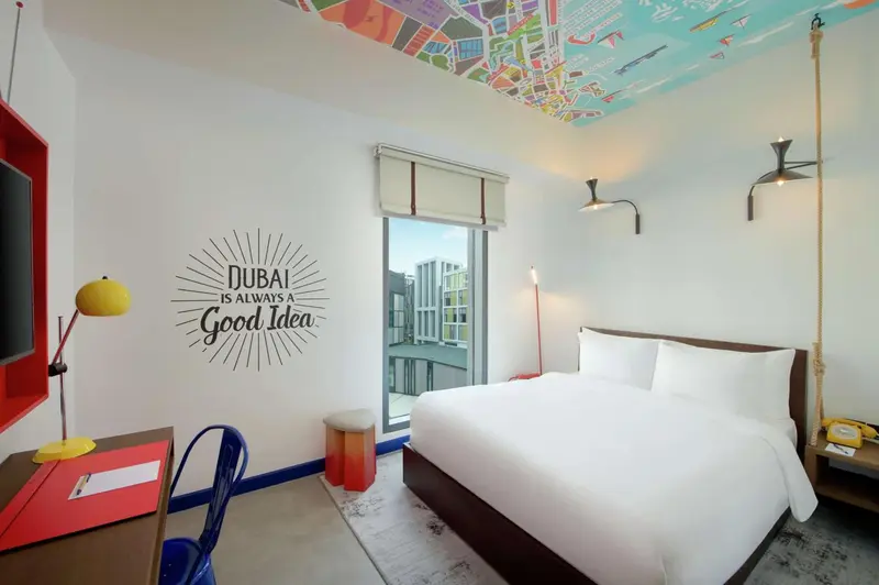 Une chambre lumineuse avec un lit blanc et une décoration murale colorée.