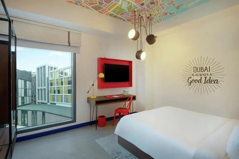Une chambre lumineuse avec un lit blanc et un bureau rouge.
