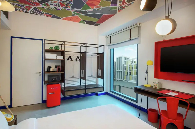 Une chambre lumineuse avec un lit blanc et un bureau rouge.