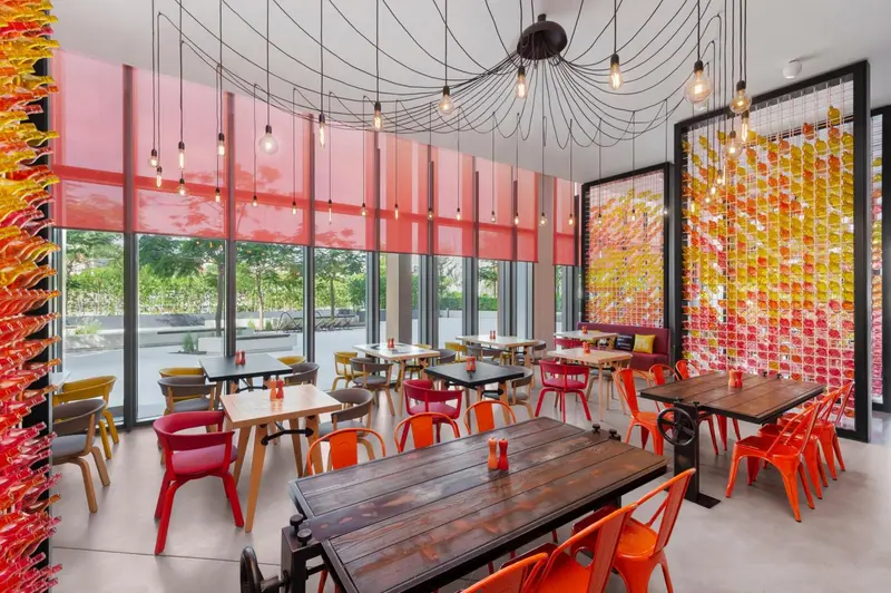 Une salle lumineuse avec des tables et des chaises colorées est décorée de suspensions et de panneaux colorés.