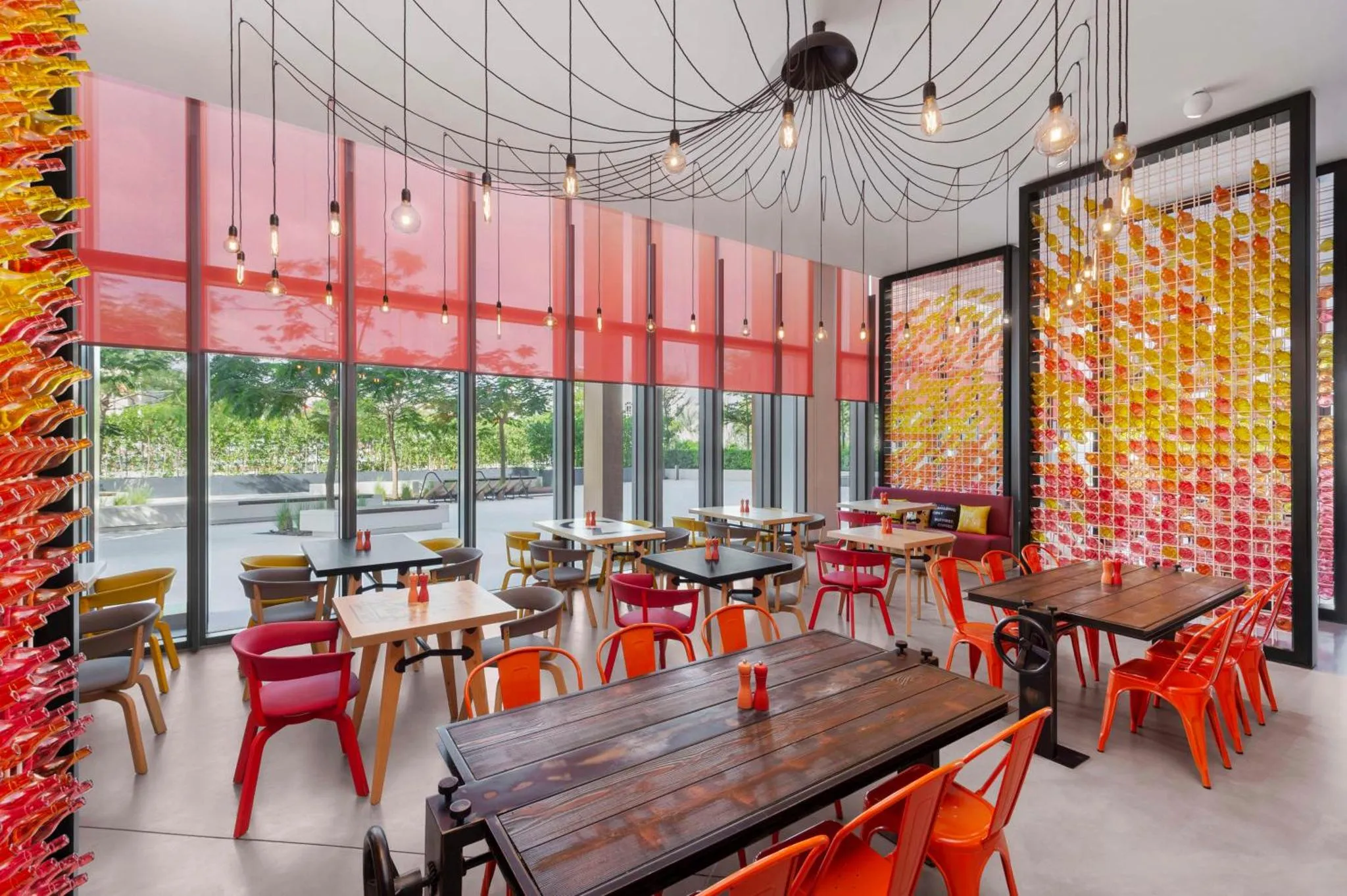 Une salle lumineuse avec des tables et des chaises colorées est décorée de panneaux colorés et éclairée par des suspensions.