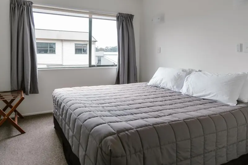 Une chambre lumineuse avec un grand lit recouvert d'une couverture grise.