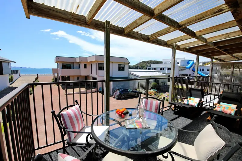 Terrasse avec mobilier de jardin et vue sur des bâtiments et la mer.