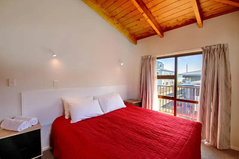 Une chambre lumineuse avec un lit recouvert d'une couverture rouge et une fenêtre donnant sur l'extérieur.