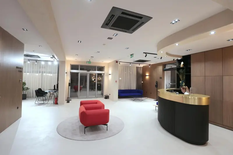 Un hall d'accueil lumineux avec un comptoir incurvé et des fauteuils rouges.