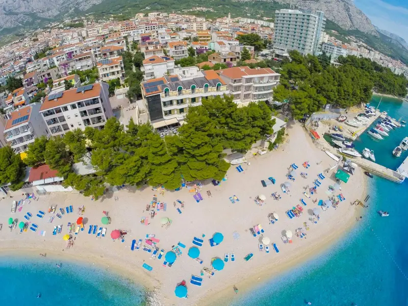 Vue aérienne d'une plage ensoleillée bordée de bâtiments et de pins.