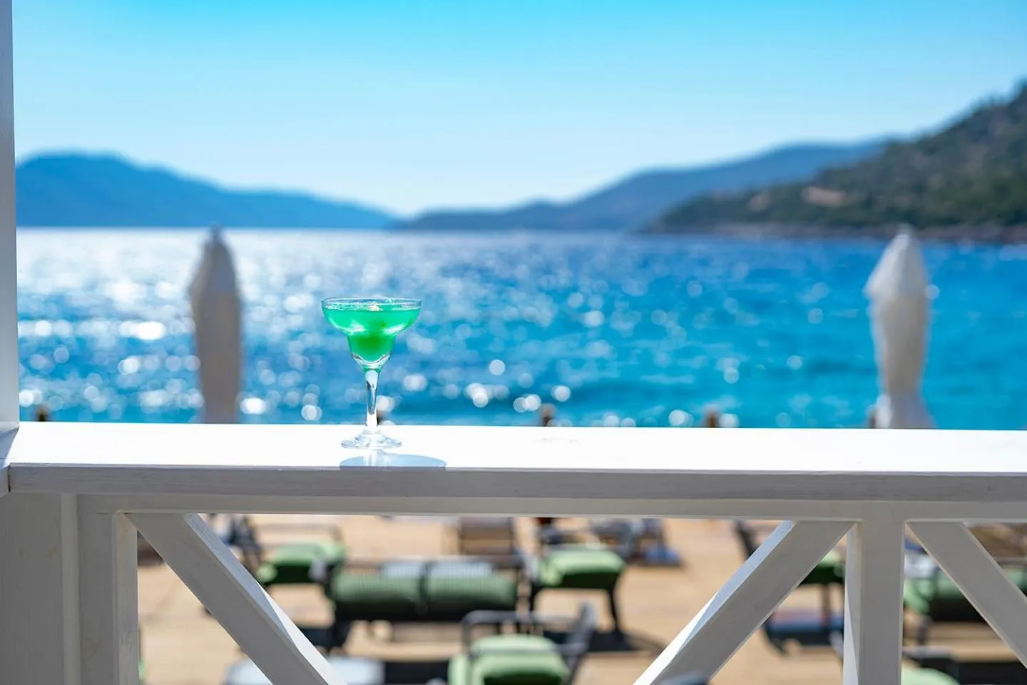 Un cocktail vert est servi sur une terrasse avec vue sur la mer.