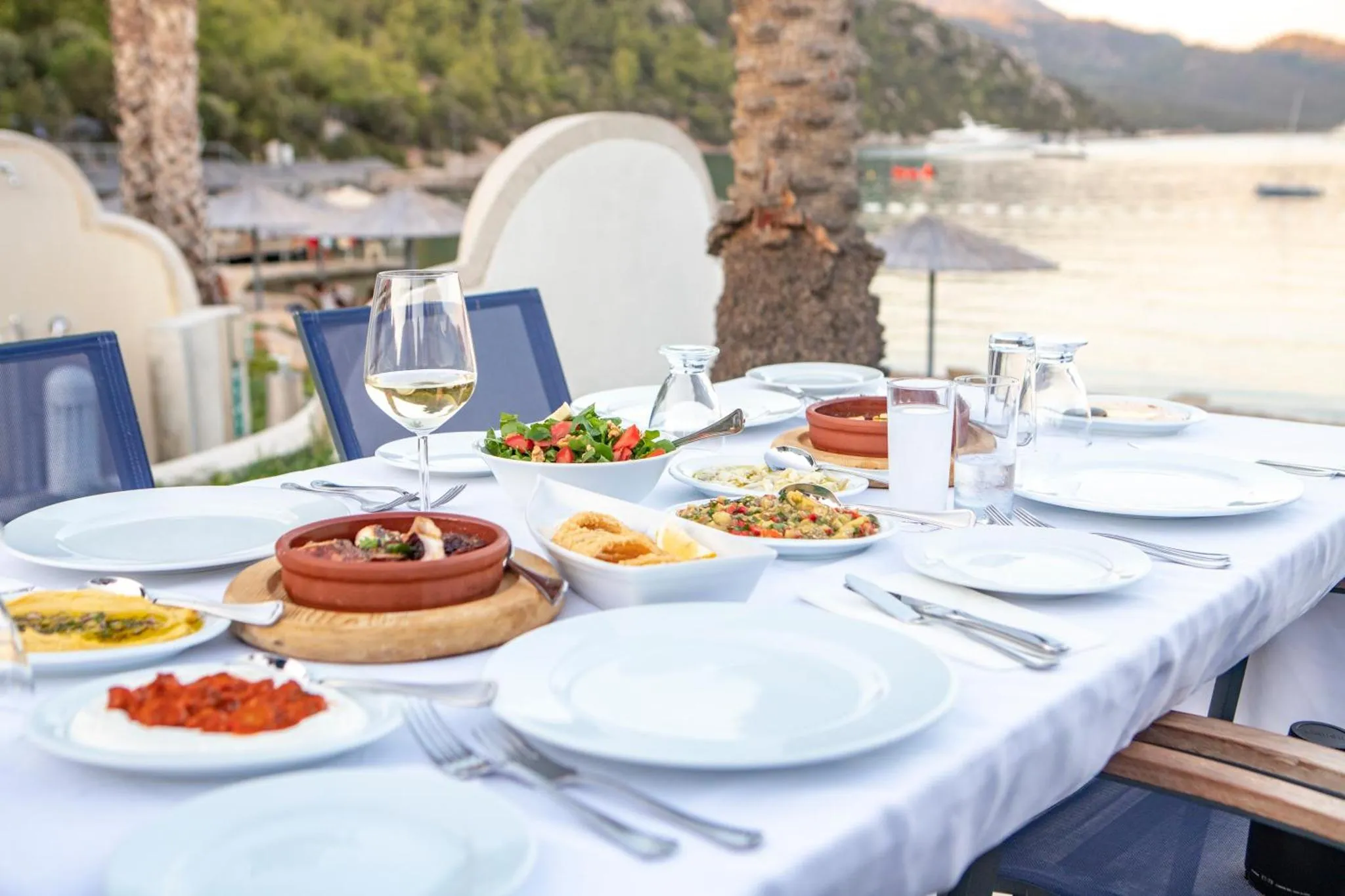 Une table dressée avec des plats et des boissons en terrasse face à la mer.