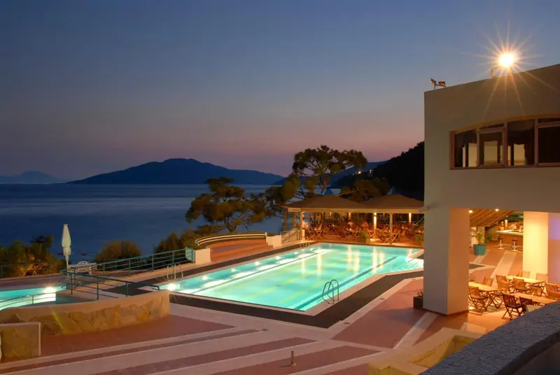 Piscine illuminée avec vue sur la mer au coucher du soleil.