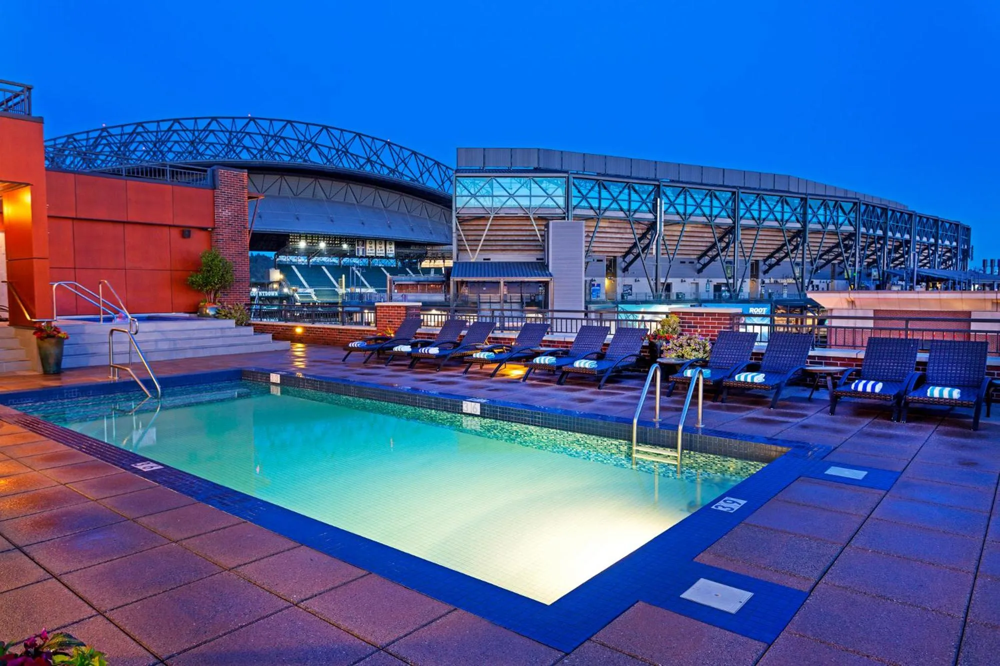 Une piscine rectangulaire avec des transats sur une terrasse en soirée.