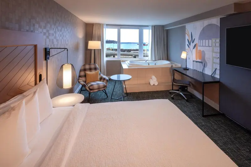 Chambre lumineuse avec un grand lit et un coin détente avec baignoire.
