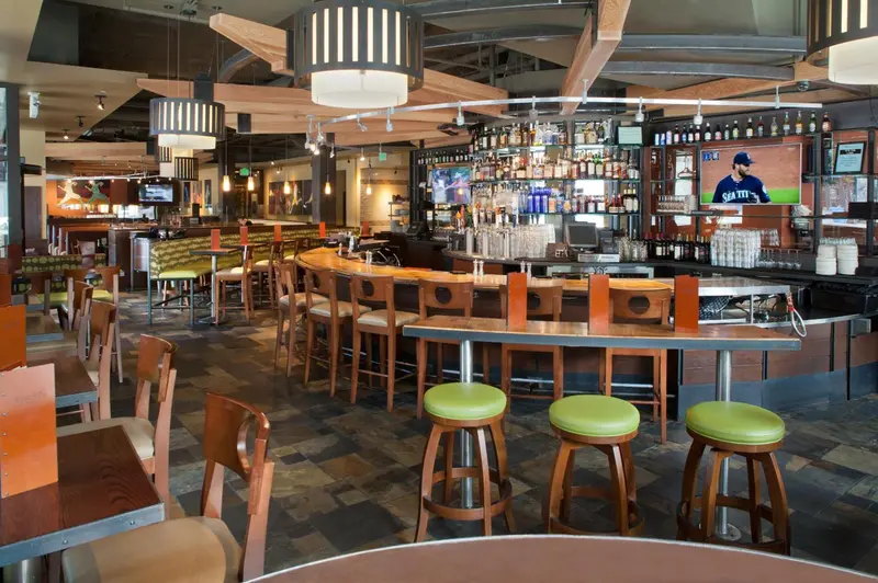 Un grand bar avec des tabourets et des tables est éclairé par des suspensions.