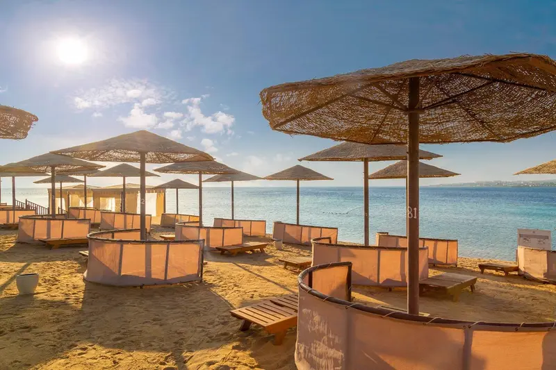 Plages ensoleillées avec des parasols en chaume et des transats sur le sable.