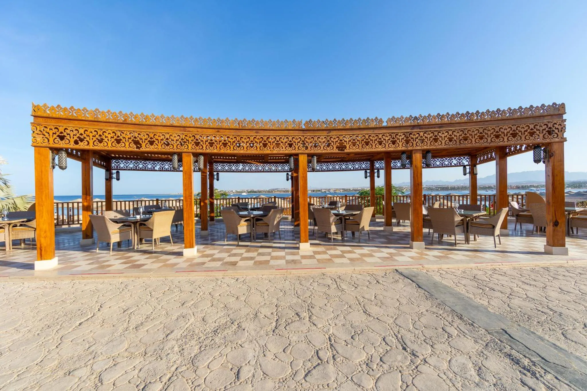 Terrasse ombragée avec tables et chaises donnant sur la mer.