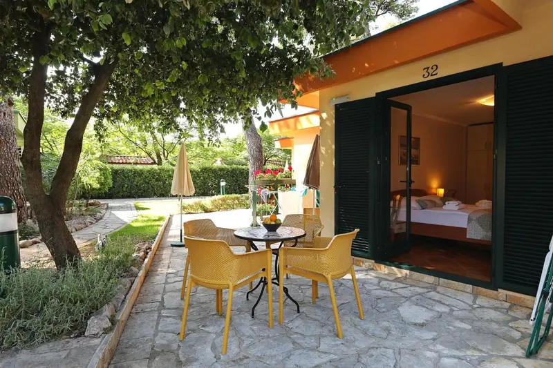 Terrasse ensoleillée avec mobilier jaune devant une ouverture sur une chambre.