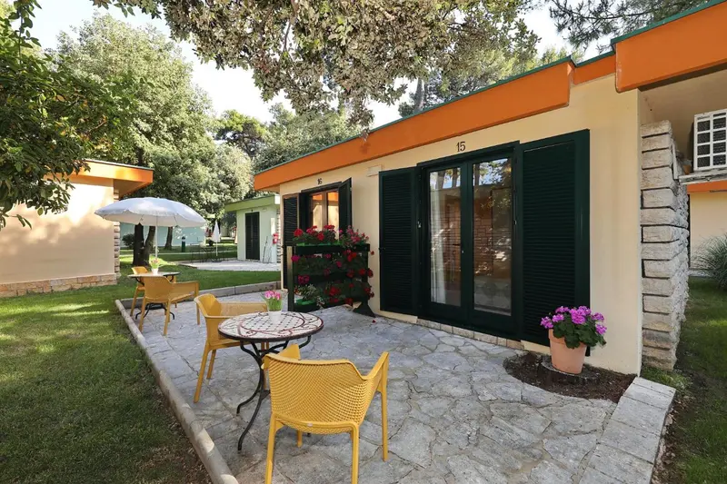 Terrasse pavée devant des logements aux volets verts et aux toits orange.