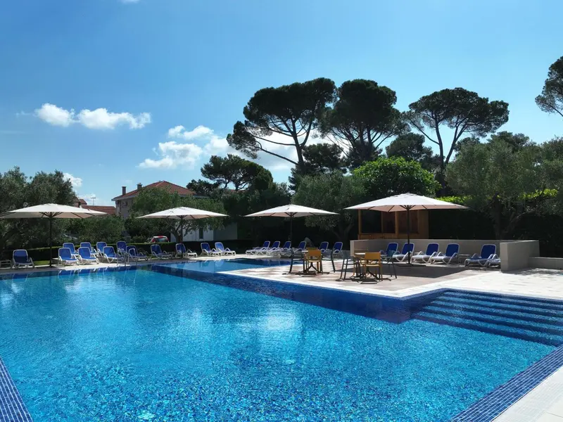 Transats et parasols bordent une piscine rectangulaire aux eaux turquoise.
