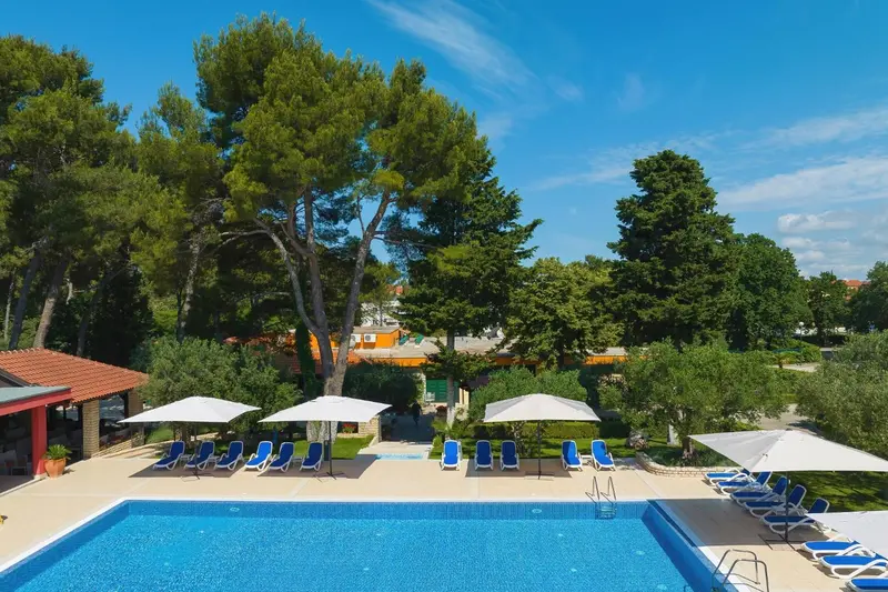 Transats blancs disposés autour d'une piscine rectangulaire sous des parasols.