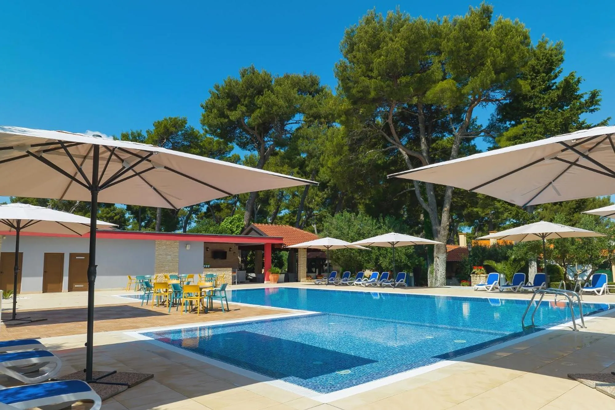 Piscine rectangulaire bordée de transats et ombragée de parasols blancs.