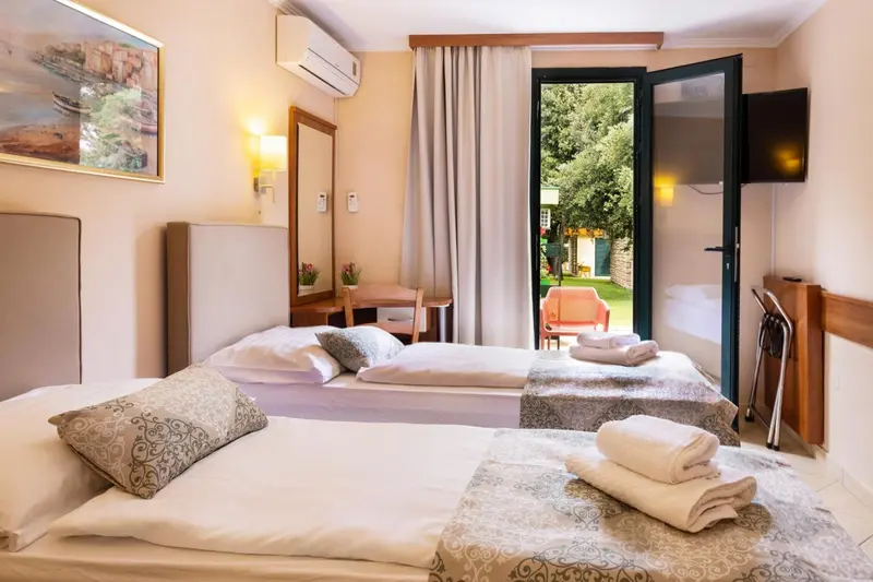 Une chambre lumineuse avec un lit double et un bureau près d'une porte-fenêtre ouverte sur un jardin.