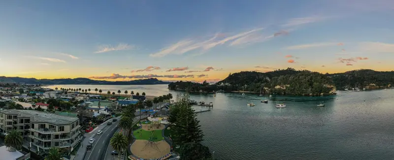 Vue aérienne d'une ville côtière au coucher du soleil, avec une plage et des bateaux amarrés dans une baie.