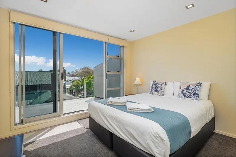 Chambre lumineuse avec un grand balcon vitré donnant sur un paysage tropical.