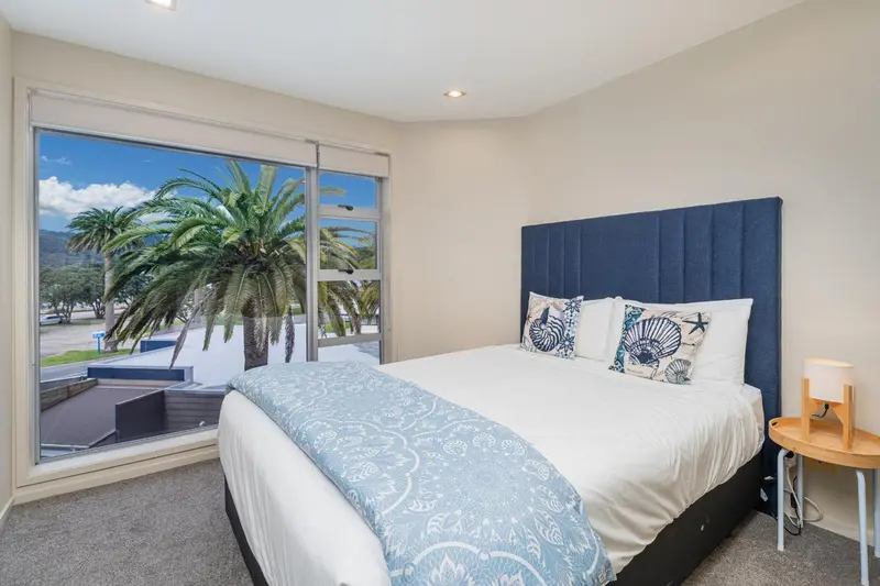 Une chambre lumineuse avec un grand lit face à une baie vitrée donnant sur une végétation tropicale.