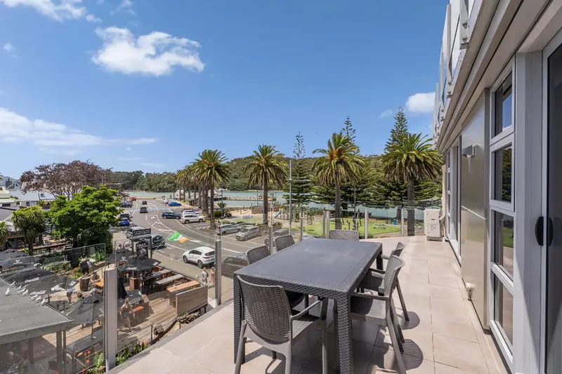 Une terrasse avec une table et des chaises offre une vue sur la végétation et un paysage urbain.