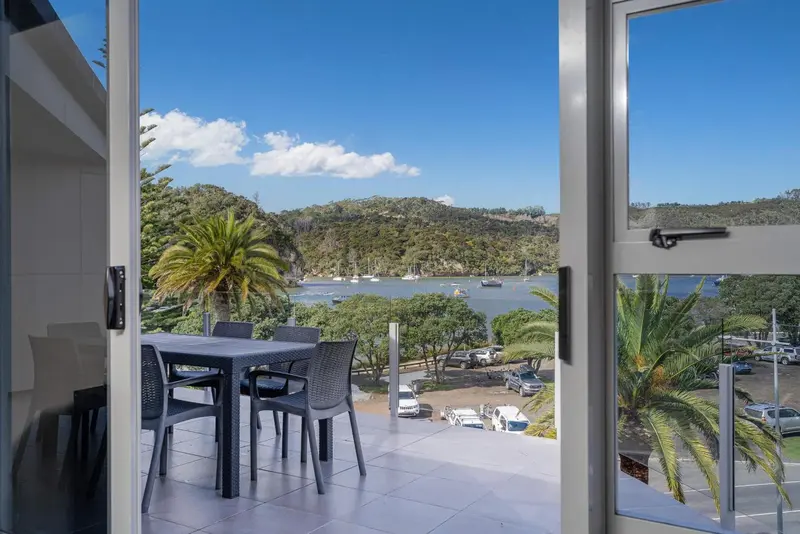 Une terrasse avec une table et des chaises offre une vue sur une baie et des collines verdoyantes.
