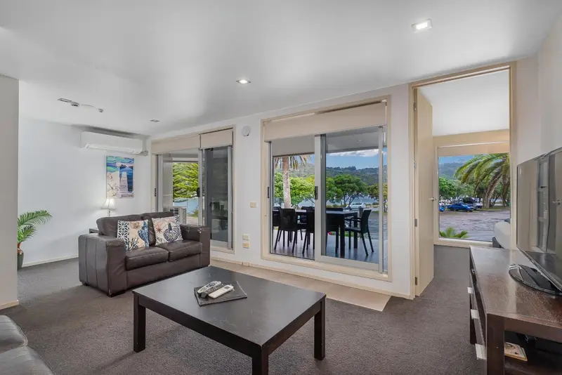 Un salon moderne avec canapé gris et vue sur la mer par de grandes baies vitrées.
