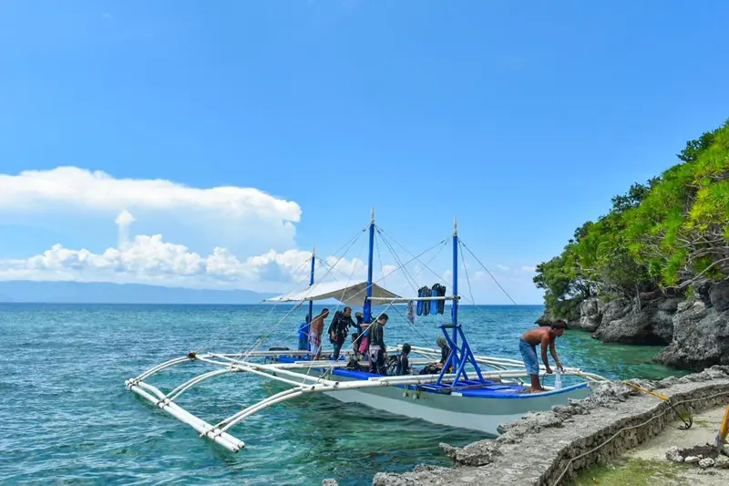 Un bateau traditionnel est amarré près d'une côte rocheuse sous un ciel bleu.