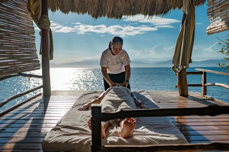 Une personne reçoit un massage sur une plateforme en bois face à la mer.