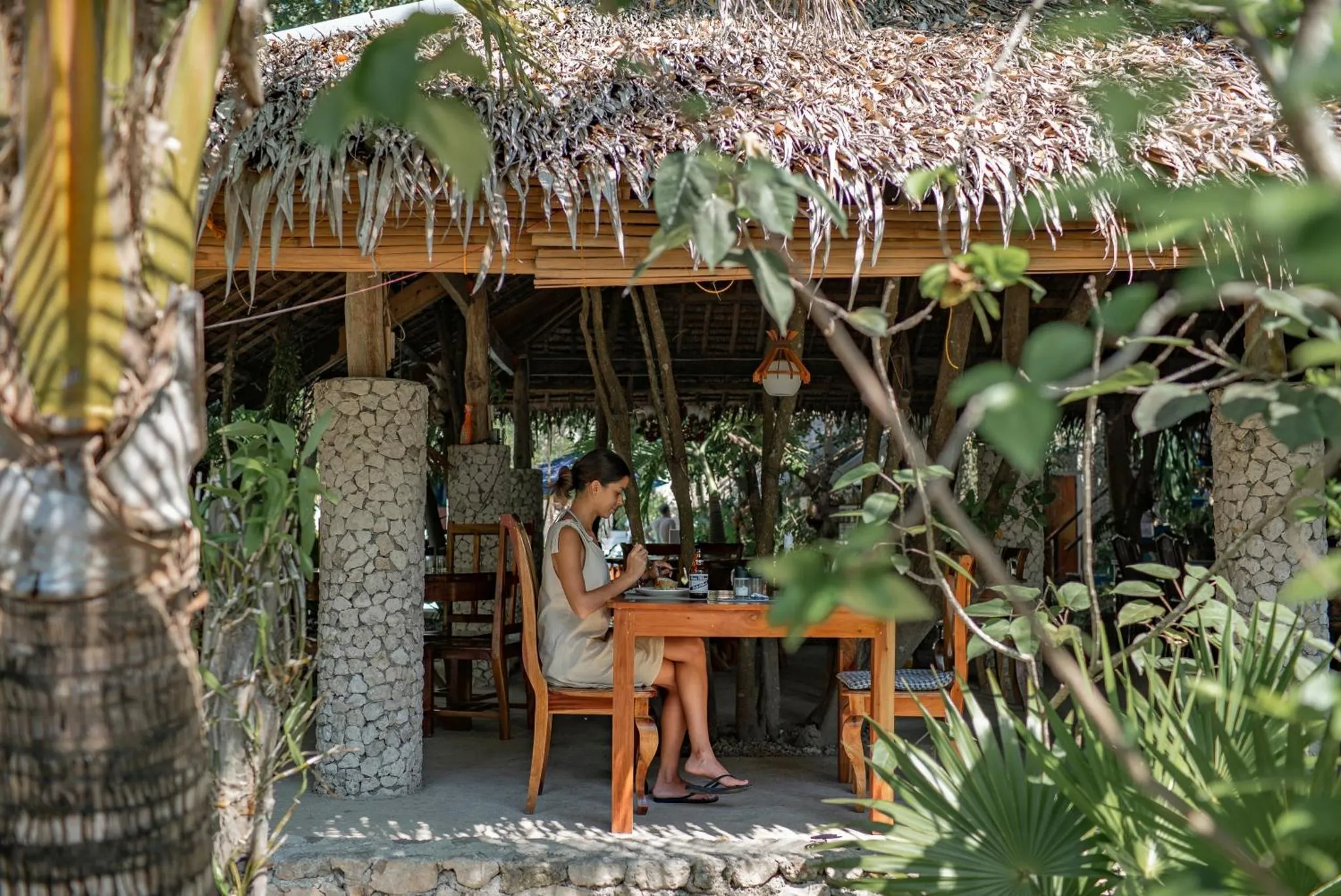 Une personne est assise à une table en bois dans un espace extérieur couvert.