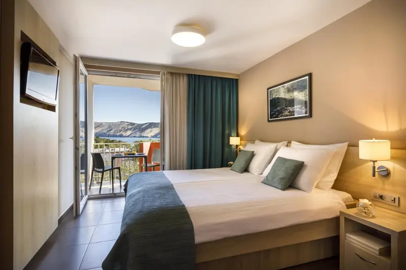 Chambre lumineuse avec un grand lit et un balcon donnant sur la mer.