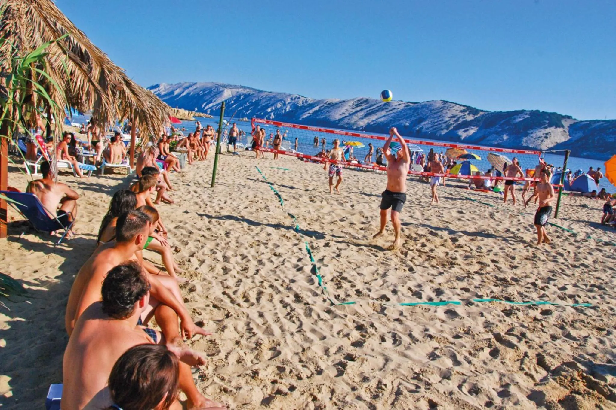 Des personnes jouent au volley-ball sur une plage de sable fin ensoleillée.