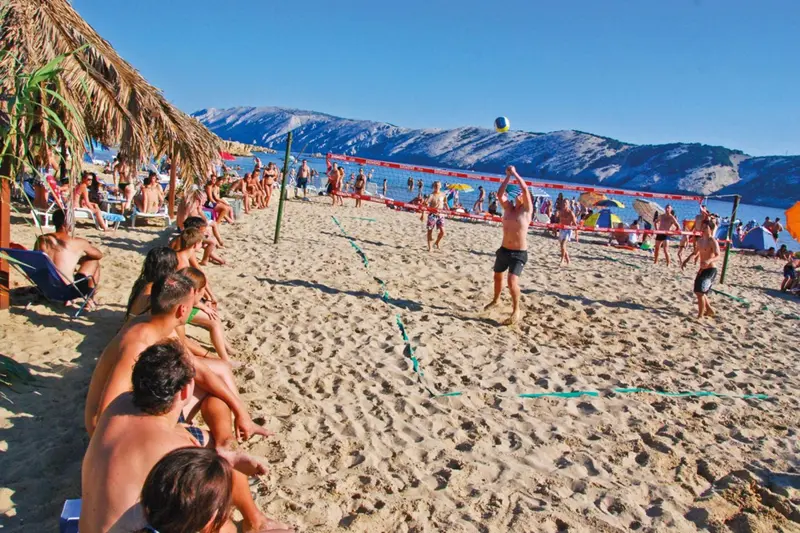 Des personnes jouent au volley-ball sur une plage de sable fin ensoleillée.
