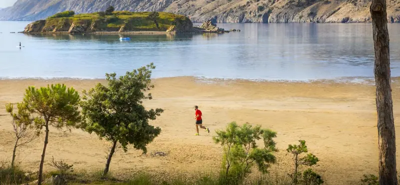Une personne court sur une plage de sable fin, avec une île en arrière-plan.