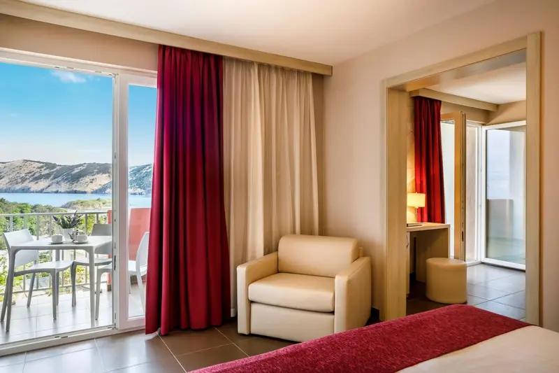 Une chambre lumineuse avec un fauteuil et un balcon offrant une vue sur la mer.