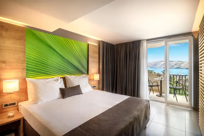 Une chambre lumineuse avec un grand lit donnant sur une vue mer via une baie vitrée.