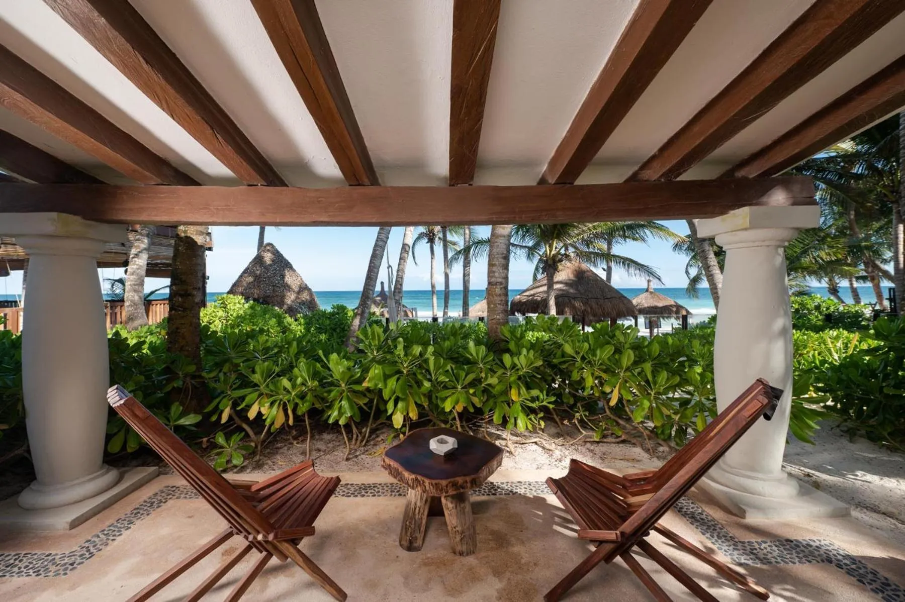 Deux fauteuils en bois invitent à la détente sur une terrasse ombragée face à la mer.
