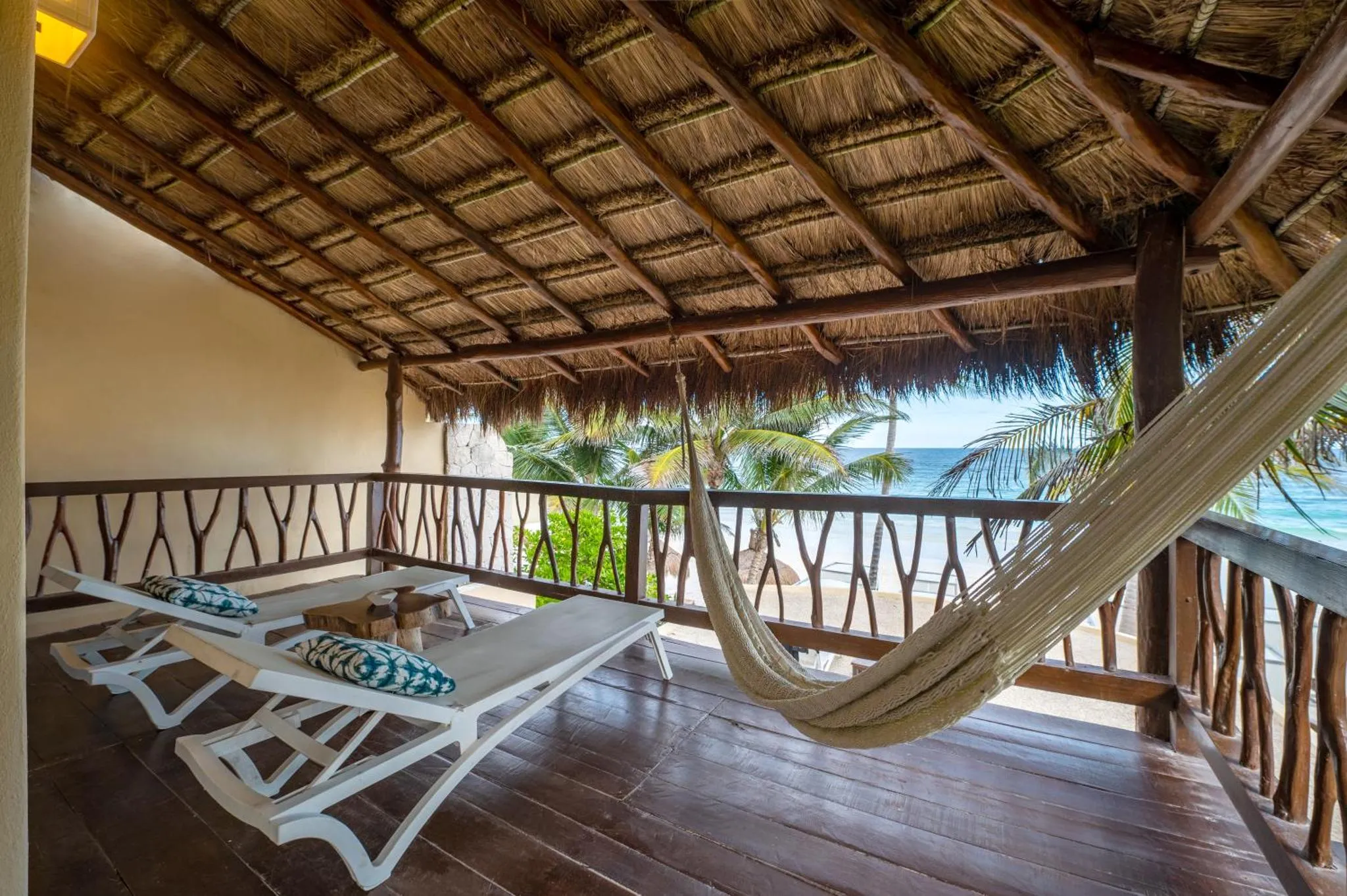 Terrasse en bois avec chaises longues et hamac donnant sur la mer.