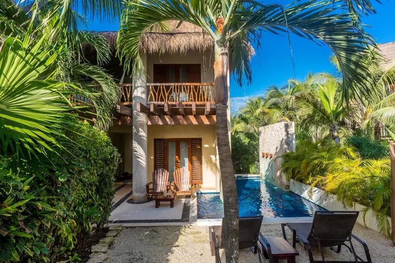 Petite maison de vacances avec piscine privée et végétation tropicale.